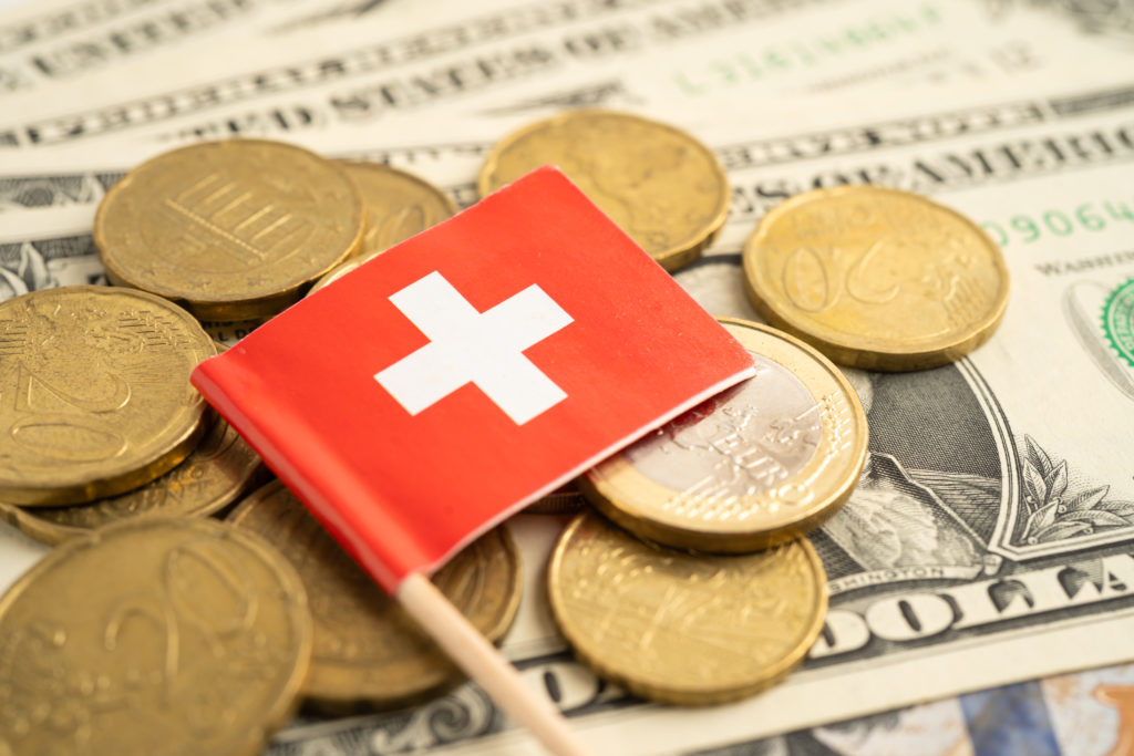 Stack of coins with Switzerland flag and US dollar banknotes.
