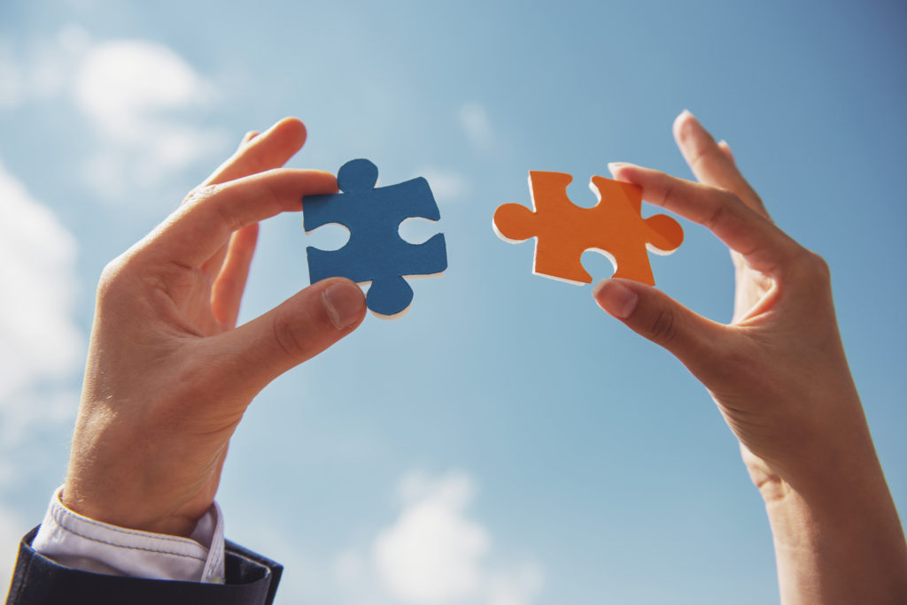 Closeup of business people wanting to put two pieces of puzzle together. Sky background.